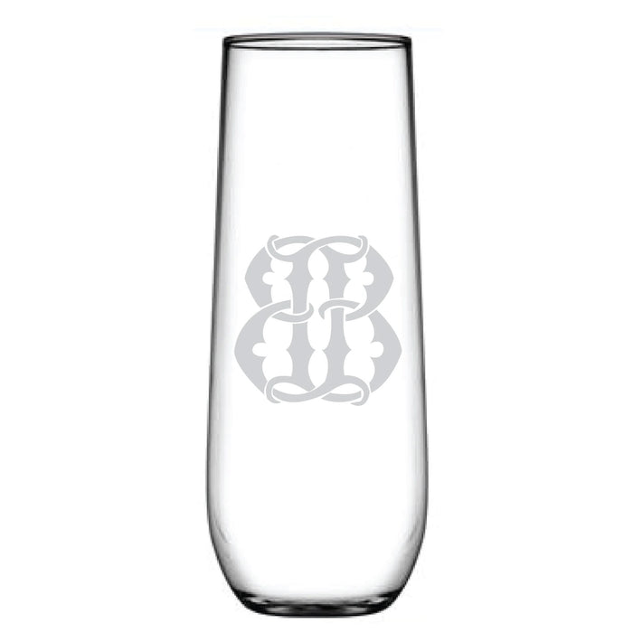 The tall, clear etched glass resembles a decorative monogram with its ornate, symmetrical design. Named the 1-Letter Monogrammed Stemless Champagne Flute, it stands elegantly empty against a white background.