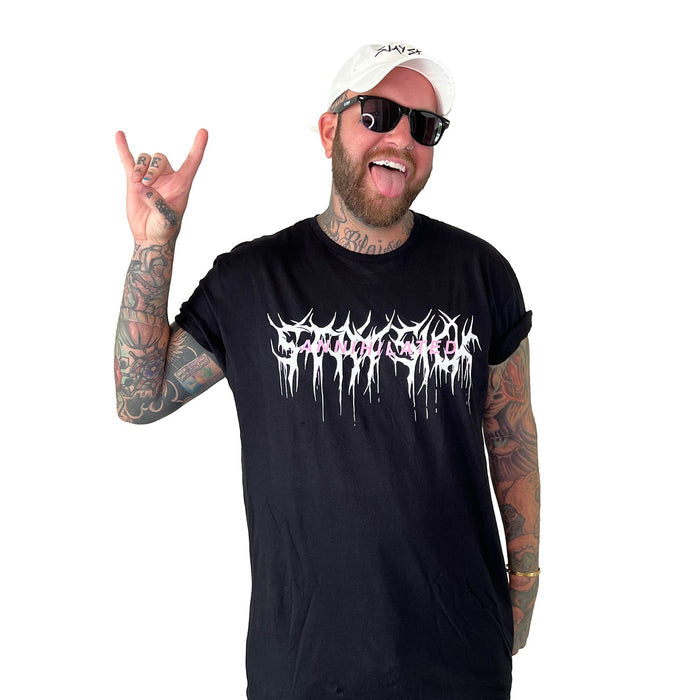 A tattooed man in sunglasses, a white cap, and a Stay Sick Clothing black T-shirt with an Annihilated graphic design smiles and flashes the rock on hand sign against a white background.