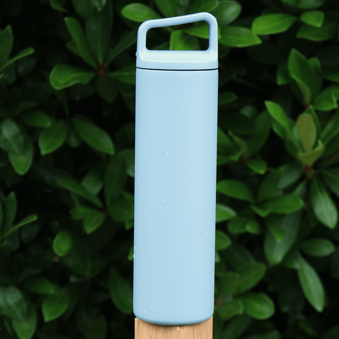 blue stainless steel water bottle on fence post with evergreen tree in the background outdoors