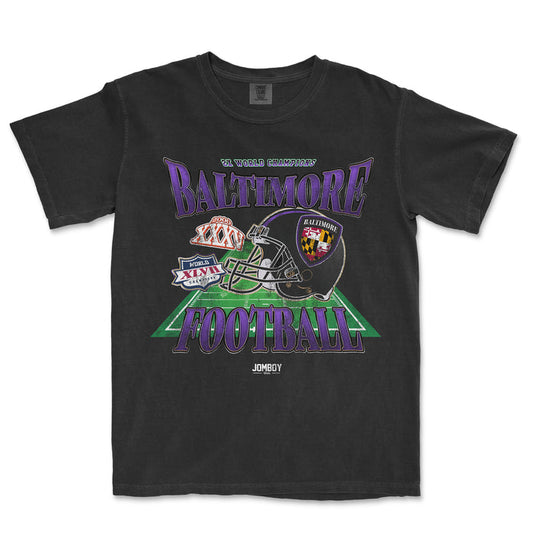 Black Comfort Colors T-shirt featuring a colorful Baltimore football graphic with helmet, patches, and "Baltimore Football" text.