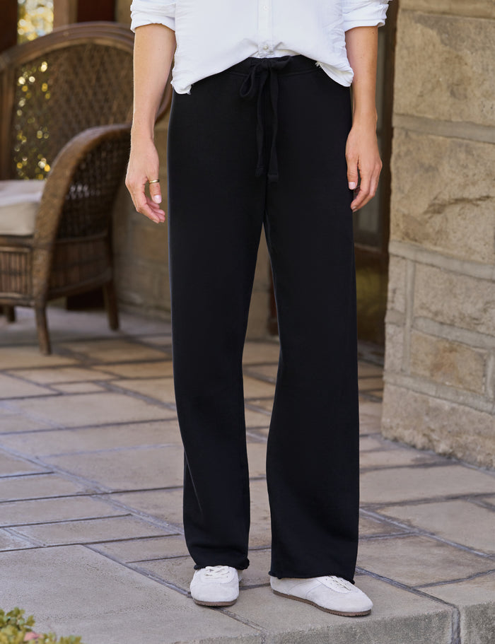 A person standing outdoors on a stone patio wearing black wide-leg drawstring pants, a white top, and white sneakers.