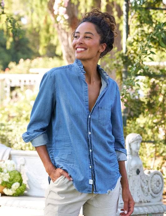 Woman wearing a blue shirt and beige shorts standing outdoors with greenery in the background