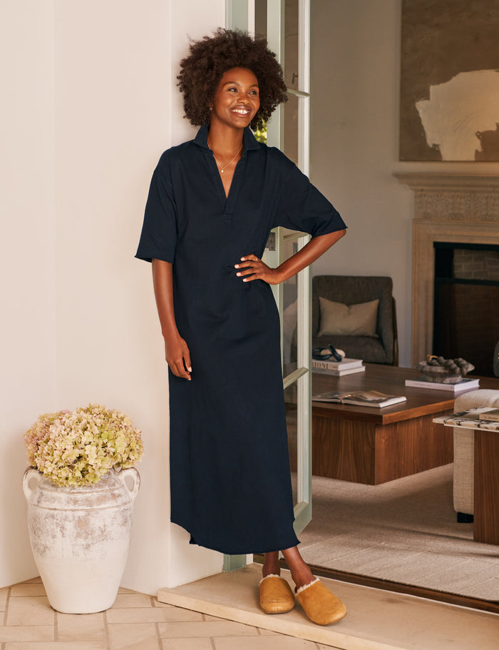 Woman in a navy dress standing in a room with a fireplace and furniture.