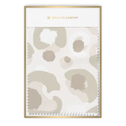 The "Fabric by the Yard - Neutral Cheetah" resembles a notepad with a white and beige abstract pattern inspired by geometric cheetah print, showcasing irregular shapes and spots. The top edge displays a perforated finish, and Emily McCarthy is elegantly inscribed at the top in gold letters.