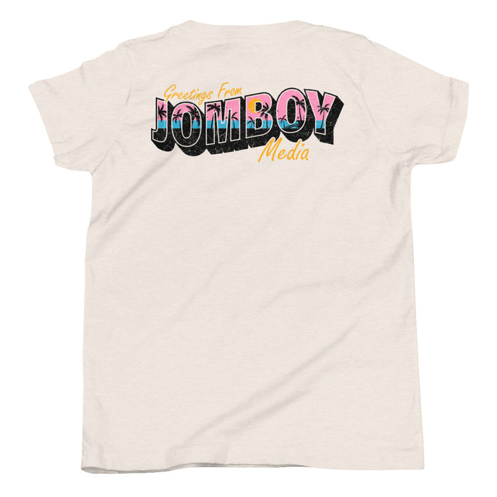 White youth T-shirt with colorful "Greetings from Jomboy Media" text, featuring pink palm trees and a black shadow effect.
