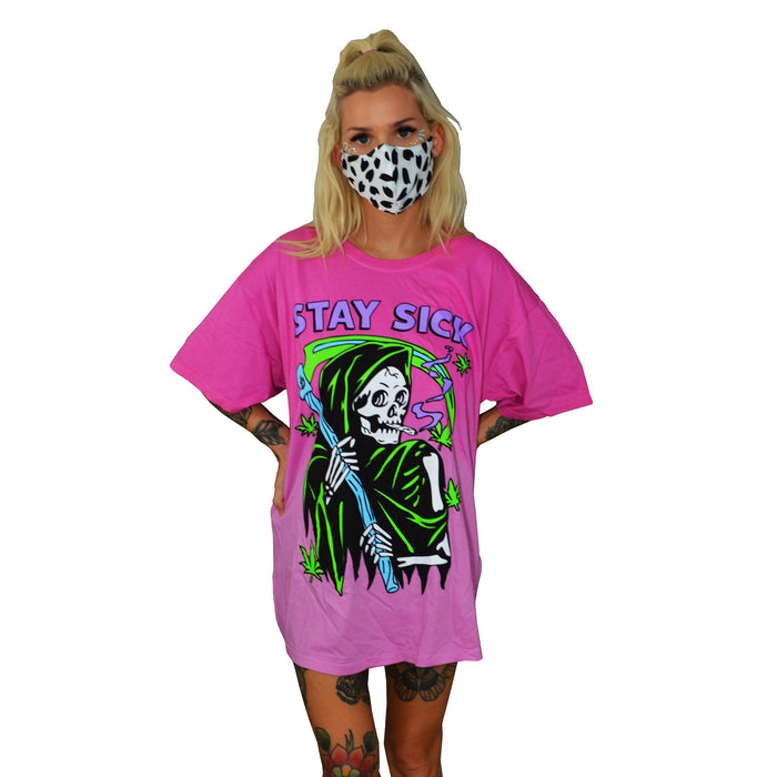 A woman wears a black-and-white spotted mask and a loose pink ombre Stay Sick Clothing T-shirt with a neon Grim Reefer, cannabis leaves, and STAY SICK text. The background is plain white.