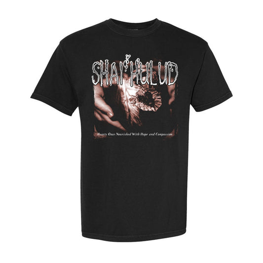 A black Shai Hulud T-shirt with stylized white SHAI HULUD text above a sepia image of hands, and “Hearts Once Nourished With Hope and Compassion.” printed below.