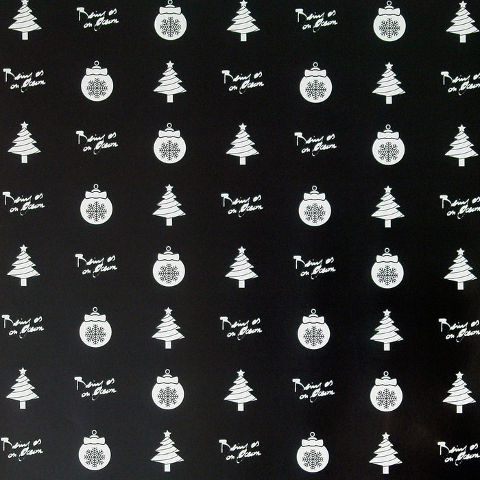 close up image of a square sheet of holiday wrapping paper. paper is black, with white christmas trees, ornaments and the words being as an ocean alternating throughout, filling the paper.