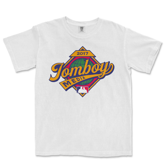White Comfort Colors T-shirt featuring a colorful 2017 Tomboy Media logo with a globe, banner, and MLB emblem.