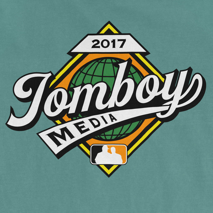 Comfort Colors teal T-shirt featuring a "Jomboy Media" logo with a globe, "2017" and a silhouette of two people at the bottom.