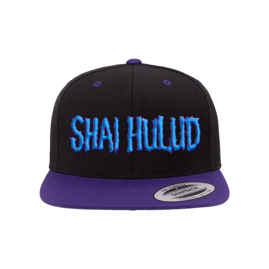 A black Shai Hulud snapback hat features a purple brim and blue embroidered SHAI HULUD text on the front, displayed against a plain black background.