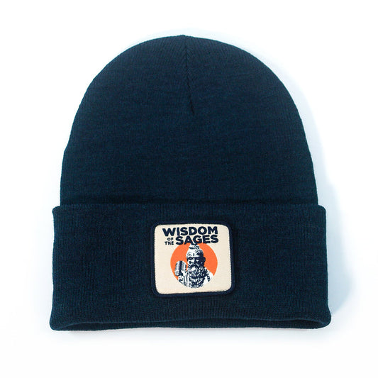 The Wisdom of the Sages black knit beanie is made with sustainable Polylana polyester and features a rectangular patch with “WISDOM OF THE SAGES” above a bearded figure and orange semicircle background. One size fits all.