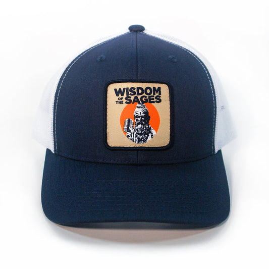 The Wisdom of the Sages retro trucker hat features navy blue and white colors, a mesh back, and a front patch with a bearded figure, microphone, and Wisdom of the Sages text on an orange circle.