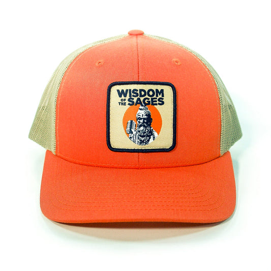 The Wisdom of the Sages trucker hat features an orange and beige design with a mesh back, snapback closure, and a front patch showing a wise man with a staff and an orange circle, plus the brand name above.