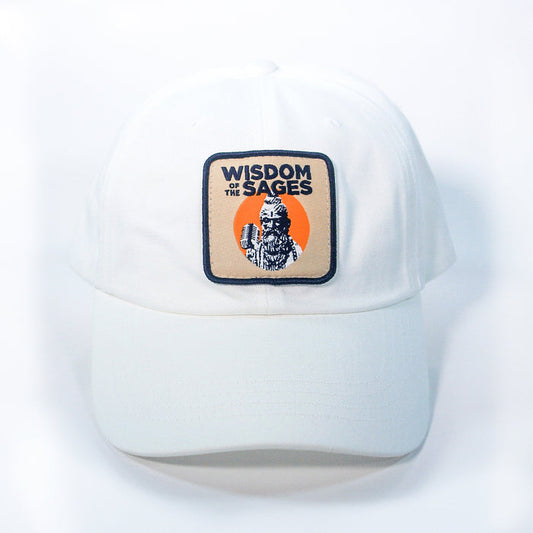 The Wisdom of the Sages Dad Hat is a white chino twill cap featuring a rectangular patch with WISDOM OF THE SAGES above an illustrated figure and orange circle, finished with a buckle closure.