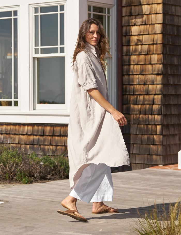 Woman in a long, light-colored dress standing on a wooden deck next to a wooden building.