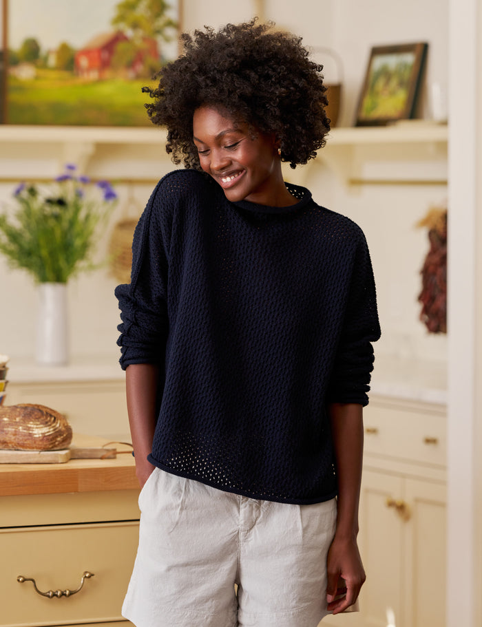 Woman wearing a navy sweater and tan shorts in a kitchen setting
