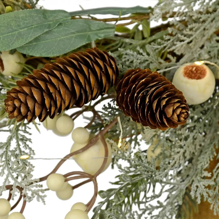 Pine cones, snowberries and green branches lit by warm white fairy lights