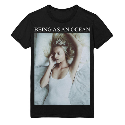 Black Tultex T-Shirt by Being As An Ocean, showing a photo of a blonde woman in a white tank top on a bed, eyes closed and arm raised. Made from preshrunk cotton with reactive-dyed fabric and “BEING AS AN OCEAN” text above the image.