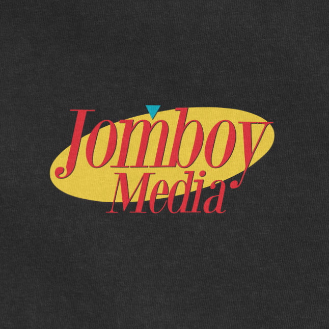 Logo for Jomboy Media with red text, yellow oval background, and a small blue triangle on a dark fabric.