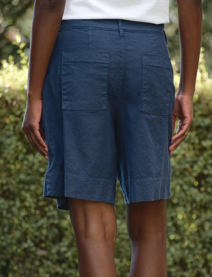 Person wearing blue shorts standing outdoors with greenery in the background